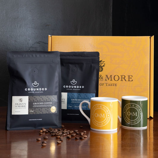 Grounded coffee packages with two mugs and coffee beans on a wooden surface.
