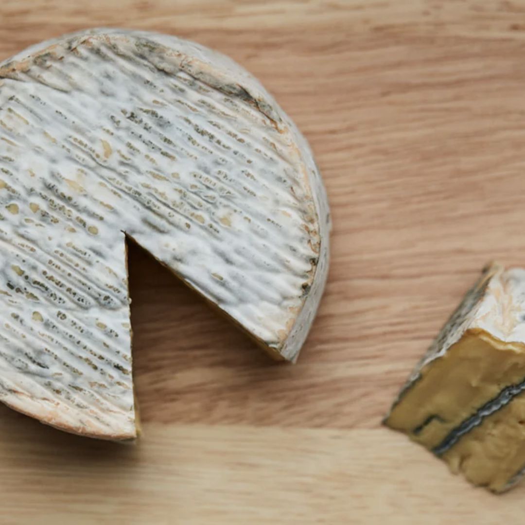 Round of Isle of White blue cheese with a slice removed on a wooden board