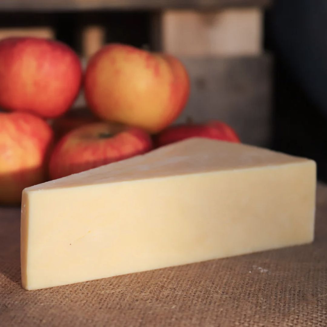 Triangle of Keens mature cheddar cheese with apples in the background on a rustic surface