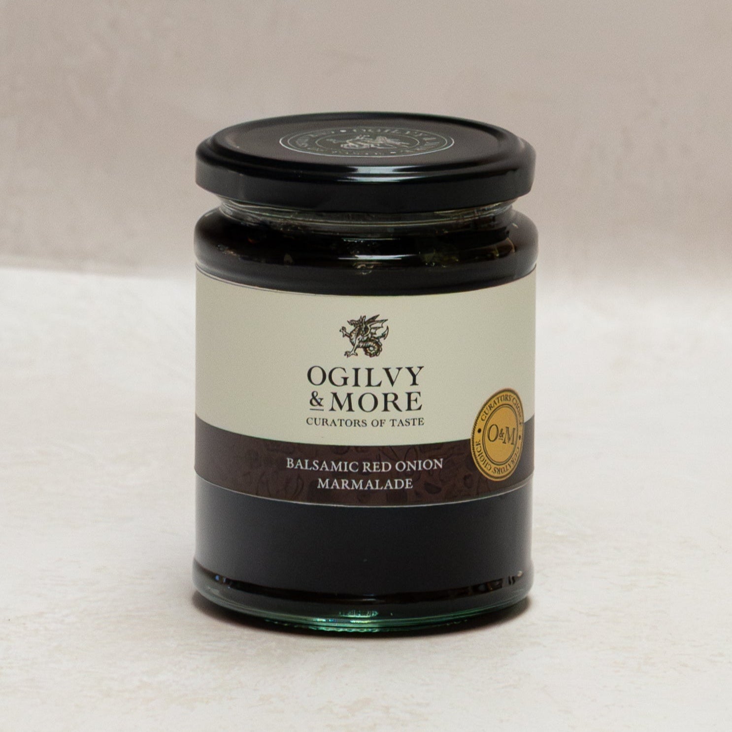 Jar of Ogily & More balsamic red onion marmalade on a white surface with a beige background