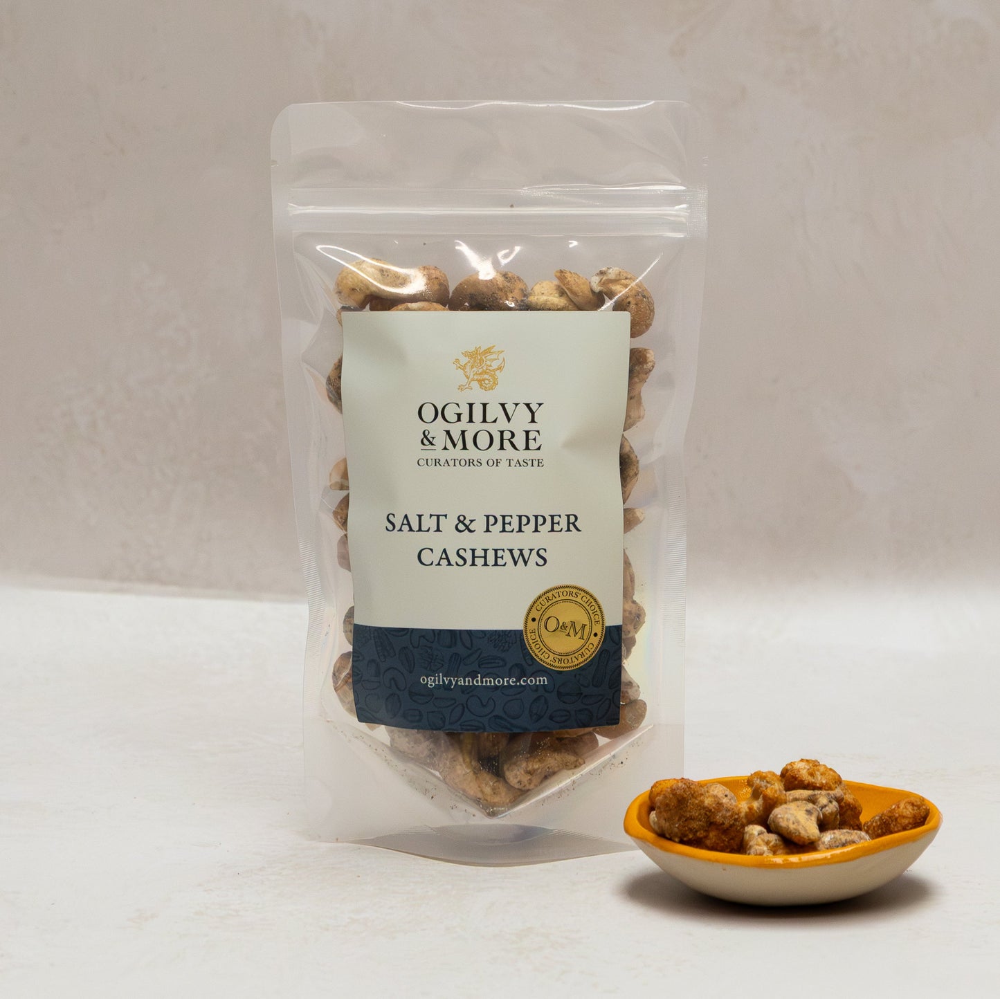 Ogilvy & More salt and pepper cashews with a small bowl of cashews on a light background