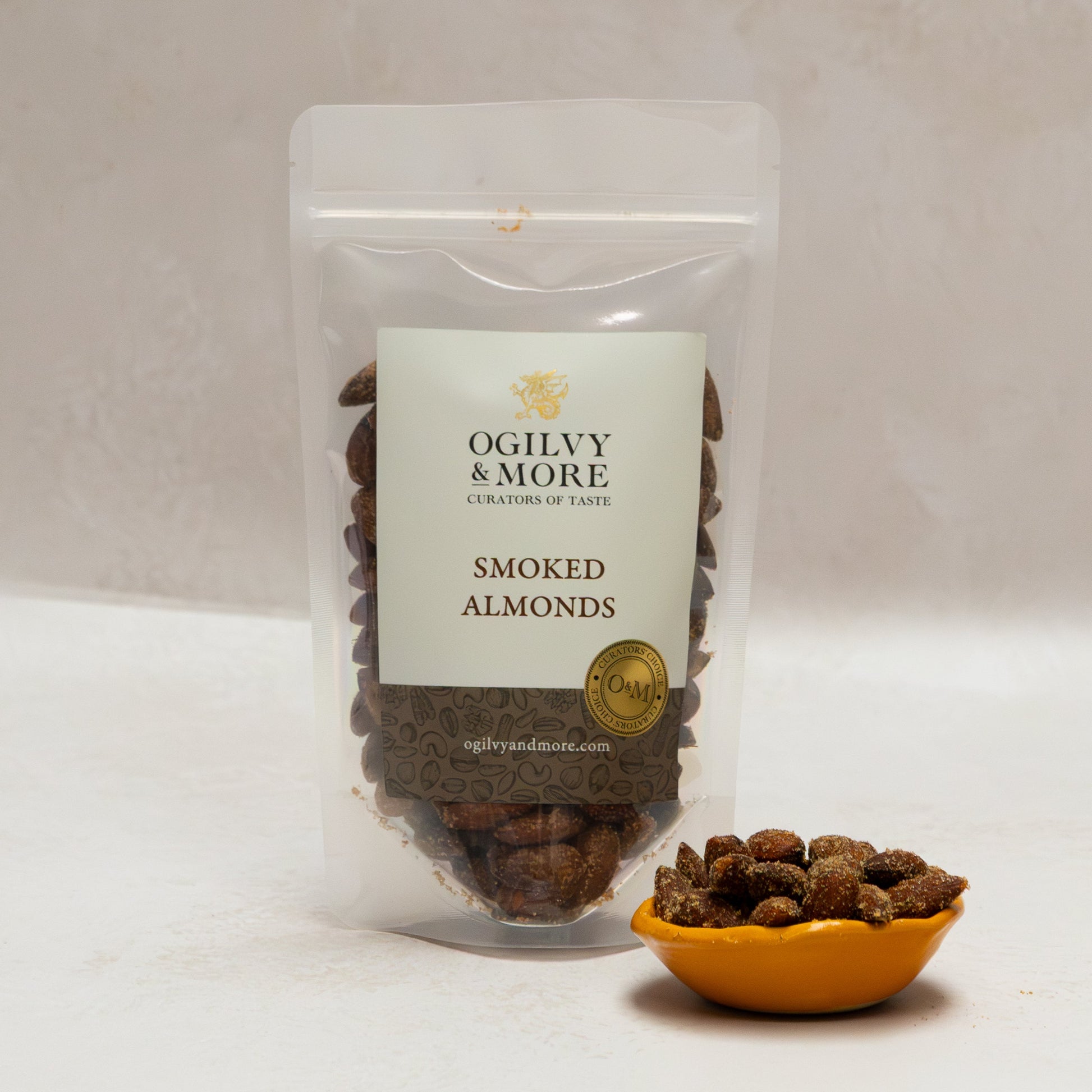 Ogilvy & More smoked almonds with a small bowl of almonds on a white background