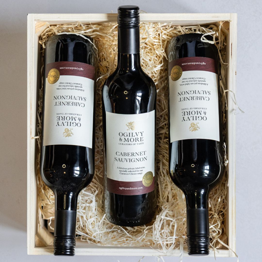 Three bottles of Ogilvy & More Cabernet Sauvignon wine in a wooden box with straw lining.