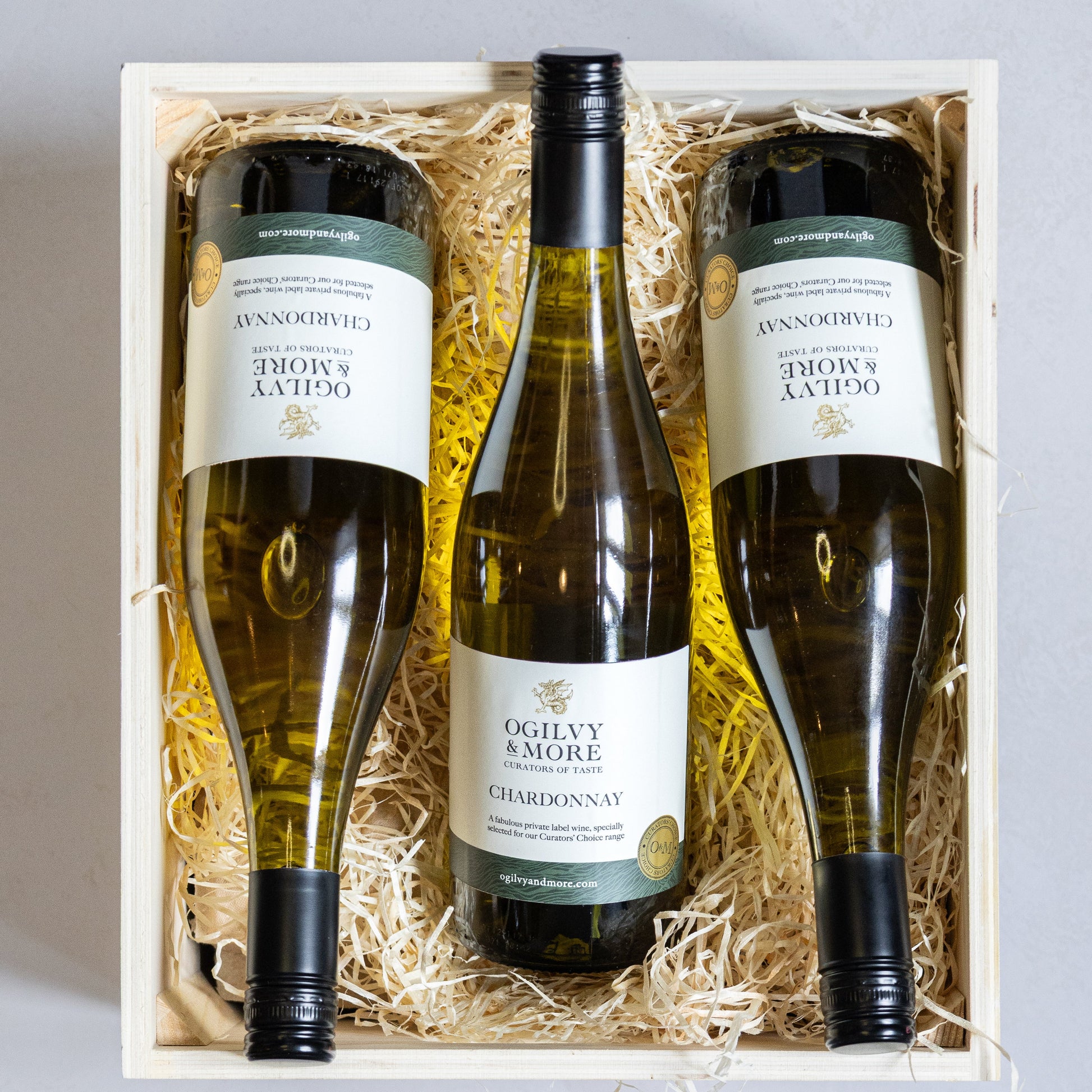 Three bottles of Ogilvy & More Chardonnay in a wooden gift box with straw interior.