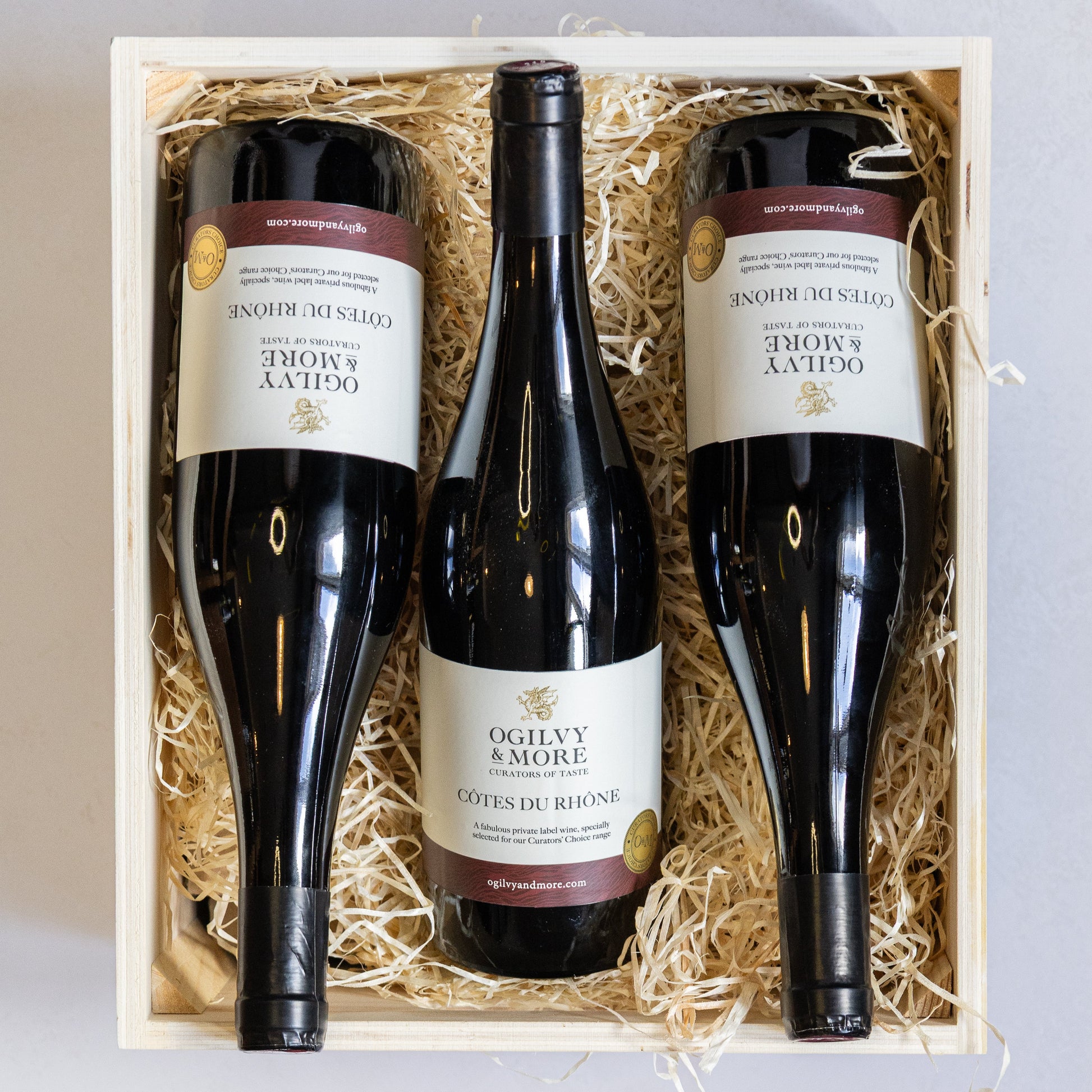 Three bottles of Ogilvy & More Cotes du Rhône wine in a wooden gift box with straw interior.