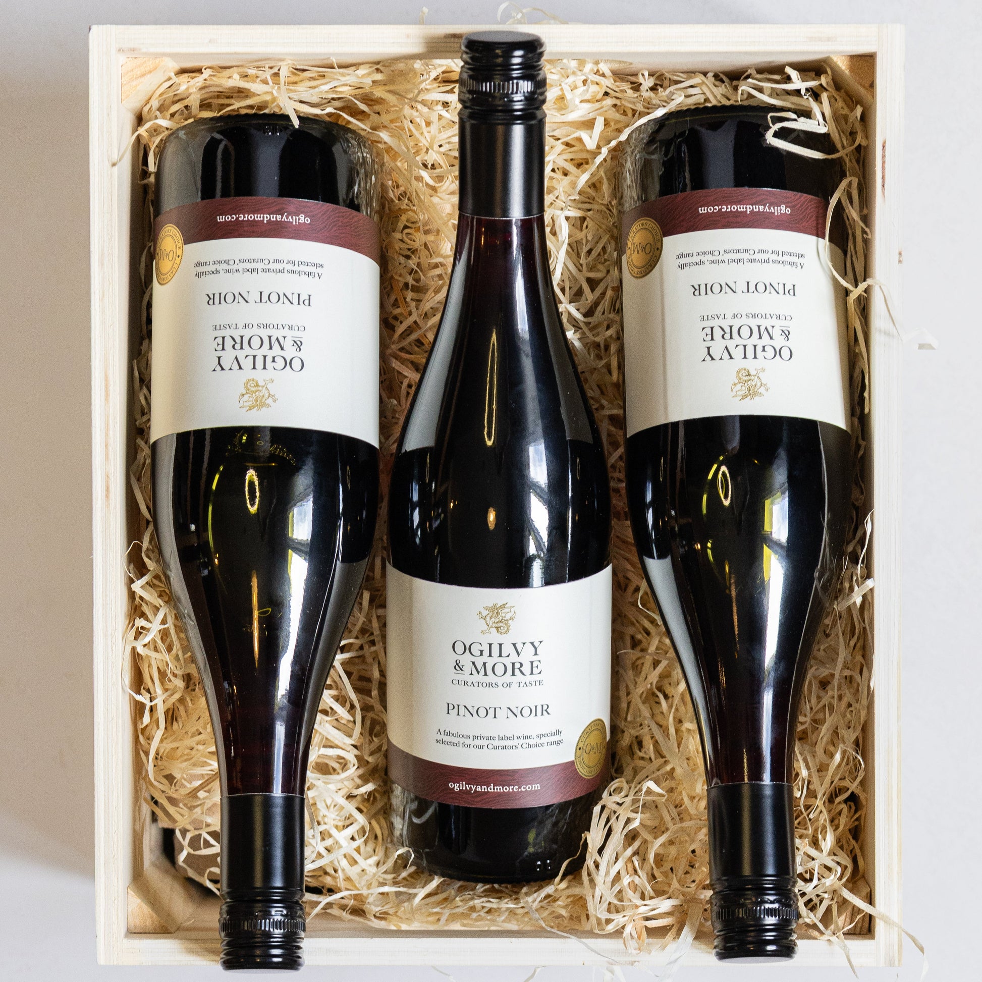 Three bottles of Ogilvy & More Pinot Noir wine in a wooden box with straw lining.