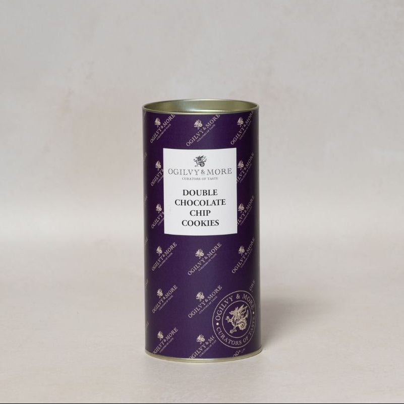 Purple cylindrical Ogilvy & More chocolate chip cookies tin with a white label on a light gray background