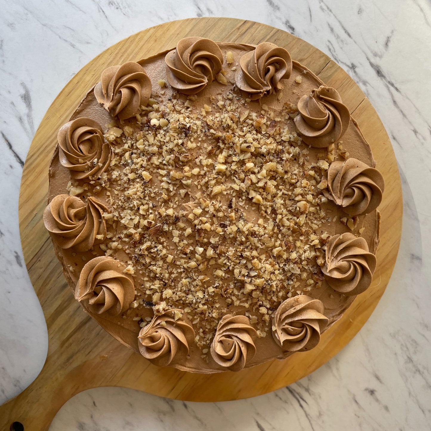 Round cake with brown frosting swirls on a wooden board against a marble background