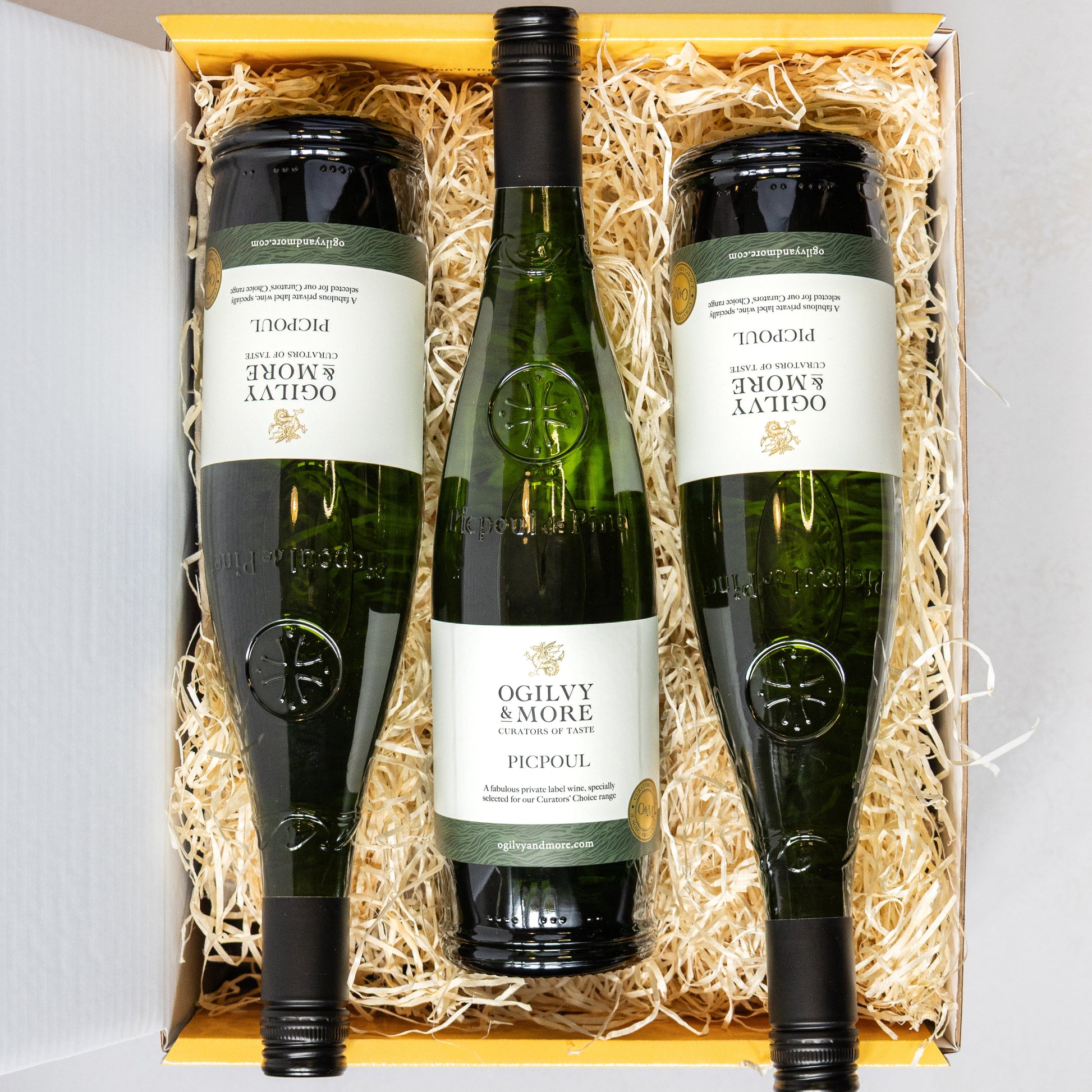 Three bottles of Ogilvy & More Picpoul wine in a wooden box with straw liner.