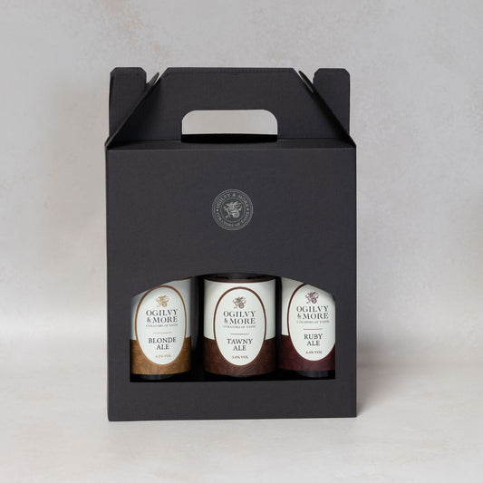 Three bottles of Ogilvy & More ale in a black gift box on a light gray background