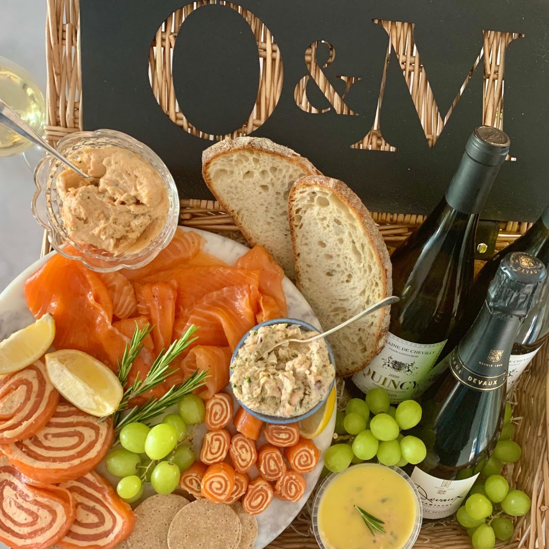 Platter of cold trout assortments, bread, and appetizers with bottles of wine on a table with 'O&M' sign.