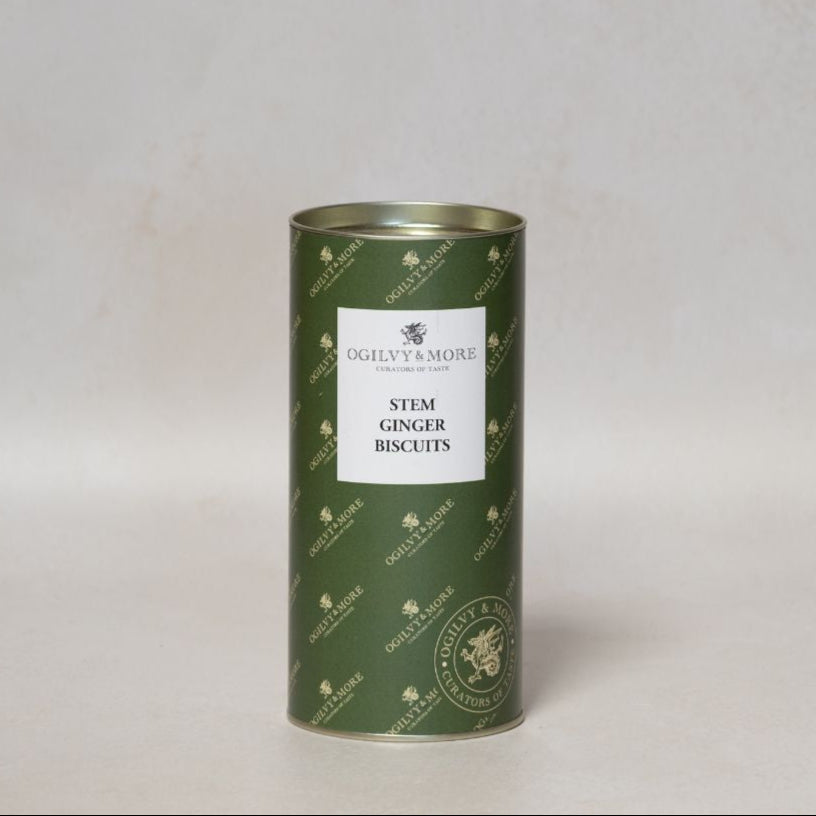 Green cylindrical tin of Ogilvy & More stem ginger biscuits on a light gray background