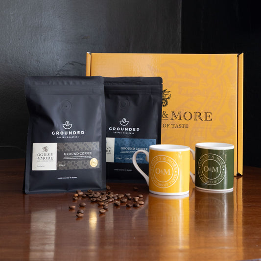 Grounded coffee packages with two mugs and coffee beans on a wooden surface.