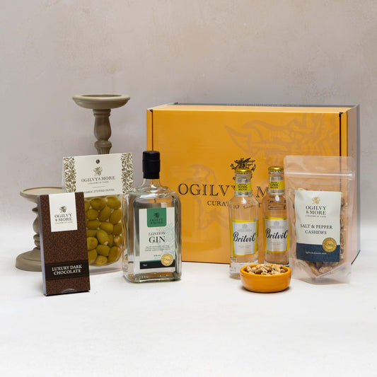 Gourmet Ogilvy & More gift set with bottles, snacks, and a box on a white surface.