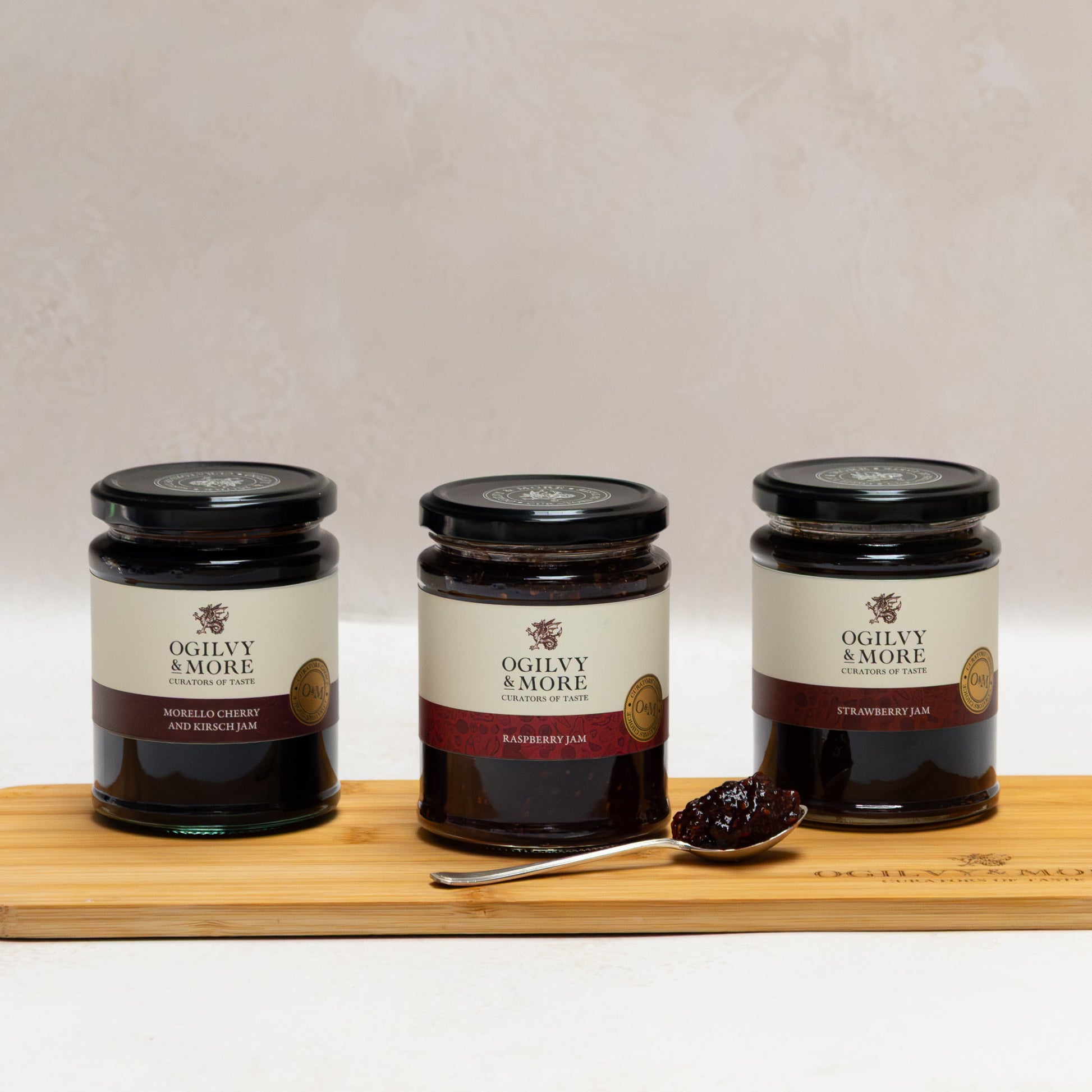 Three jars of Ogilvy & More jam on a wooden board with a white background