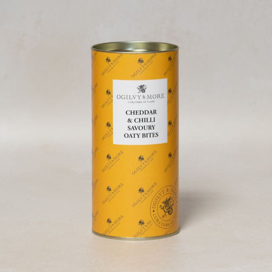 Yellow tube of Ogilvy & More Cheddar & Chilli Savoury Oaty Bites with a label on a light gray background