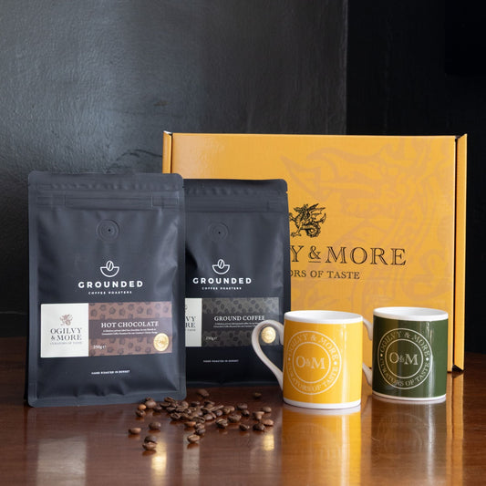 Coffee packaging and mugs with 'Ogilvy & More' branding on a dark background