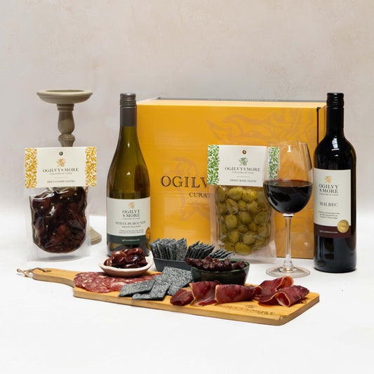 Ogilvy and More wine and charcuterie set with two bottles of wine, a charcuterie board, and a glass of red wine on a white background.