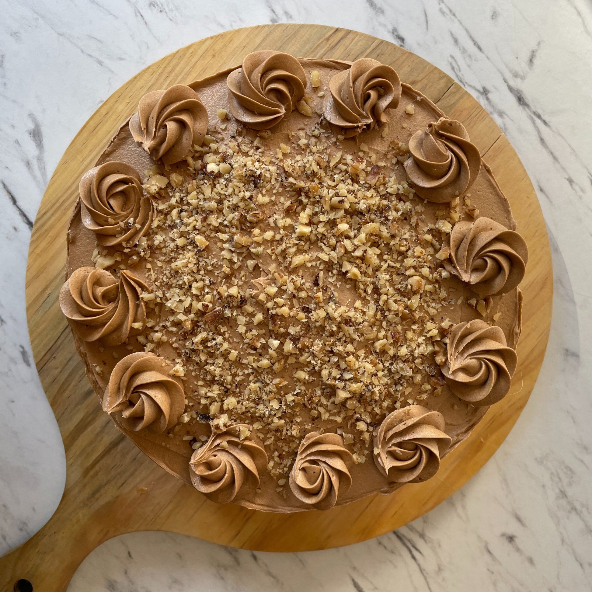 Round cake with brown frosting swirls on a wooden board against a marble background