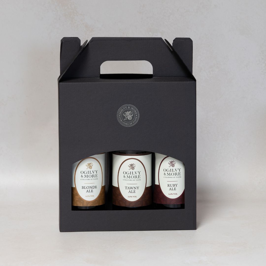 Three bottles of Ogilvy & More ale in a black gift box on a light gray background